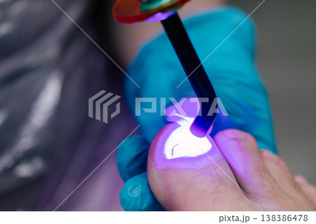 UV Lamp Curing Gel Polish on Toenail: Professional Pedicure Procedure with LED Light in Beauty Salon. Close-up view of professional pedicure procedure showing nail Bright purple light illuminates the  138386478