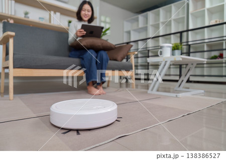 Woman with tablet observing robotic vacuum in living room Woman with tablet observing robotic vacuum in living room 138386527