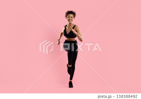 Sporty black woman running toward camera in activewear on pink studio background 138388492
