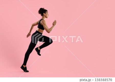 Young sporty black woman running in place in activewear on pink background Young sporty black woman running in place in activewear on pink background 138388570