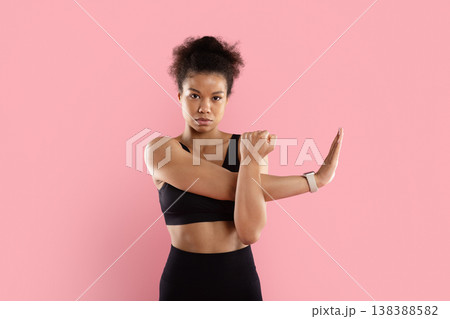 Focused black sportswoman stretching arm across chest with serious expression 138388582