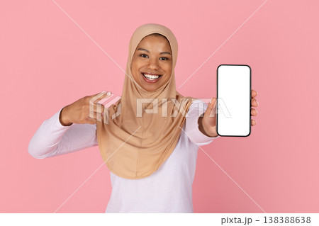 Young black Muslim woman in hijab pointing finger at blank smartphone screen 138388638