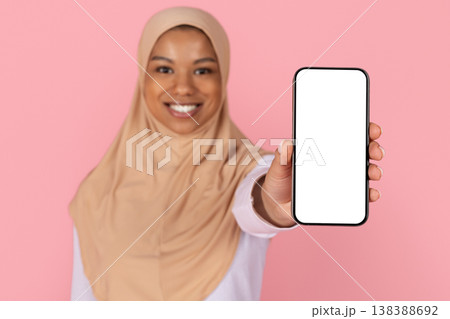 Young black Muslim woman in hijab extending blank screen smartphone toward camera Young black Muslim woman in hijab extending blank screen smartphone toward camera 138388692
