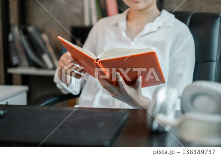 Individual reading an orange book at a desk in a contemporary office environment. Individual reading an orange book at a desk in a contemporary office environment. 138389737