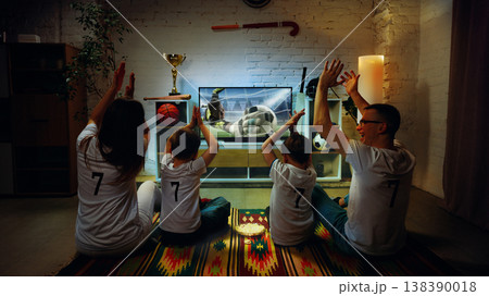 Family reacting to football save on TV at home clapping and raising hands together. Family reacting to football save on TV at home clapping and raising hands together. 138390018