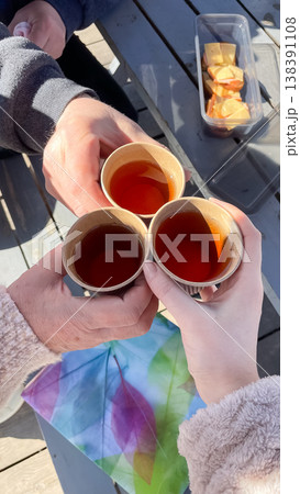 Top view of three people clinking paper cups with tea in a toast during a sunny spring outdoor picnic Top view of three people clinking paper cups with tea in a toast during a sunny spring outdoor picnic 138391108