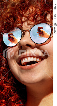 Close up woman with red curly hair and beer glasses reflected in sunglasses smiling. Close up woman with red curly hair and beer glasses reflected in sunglasses smiling. 138391827