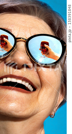 Senior woman in sunglasses with dark beer glass reflected in lenses smiling outdoors Senior woman in sunglasses with dark beer glass reflected in lenses smiling outdoors 138391848