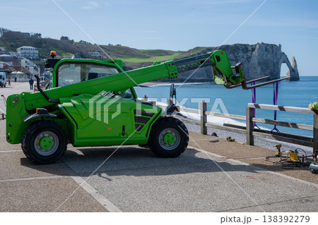 Construction machinery working on seaside promenade with green telehandler and coastal cliffs landscape in Etretat France renovation concept 138392279