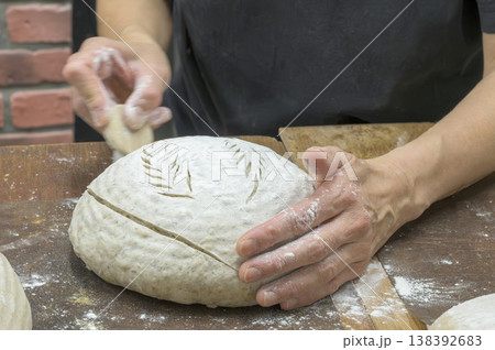 バヌトン（発酵カゴ）から出したカンパーニュ生地にクープを入れるパン職人の手元 138392683