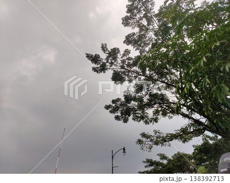 Dark clouds gather above lush trees, hinting at rain on a quiet, overcast afternoon. 138392713
