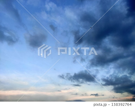 A calm sky at dusk with scattered clouds and a soft moon glowing in the serene blue horizon. 138392764