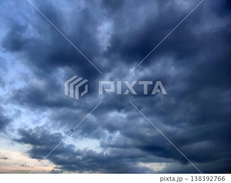 A calm sky at dusk with scattered clouds and a soft moon glowing in the serene blue horizon. 138392766