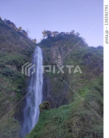 Tall waterfall cascading down lush green cliffs under sunlight, creating a serene and majestic view. Tall waterfall cascading down lush green cliffs under sunlight, creating a serene and majestic view. 138392791