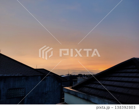 Sunset over rooftops and mountains warm hues meet silhouettes in a peaceful urban horizon Sunset over rooftops and mountains warm hues meet silhouettes in a peaceful urban horizon 138392803