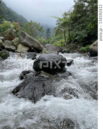 Crystal-clear river flowing over smooth rocks, framed by lush forest and misty mountain views. 138392812