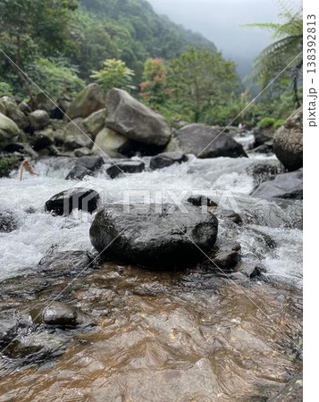 Crystal-clear river flowing over smooth rocks, framed by lush forest and misty mountain views. Crystal-clear river flowing over smooth rocks, framed by lush forest and misty mountain views. 138392813