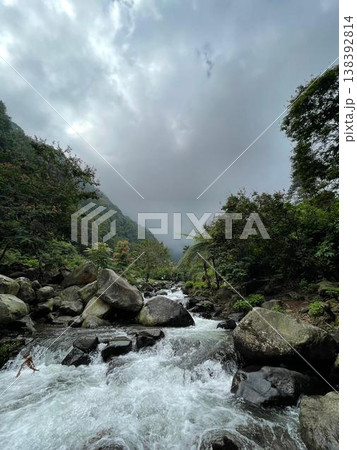 Crystal-clear river flowing over smooth rocks, framed by lush forest and misty mountain views. Crystal-clear river flowing over smooth rocks, framed by lush forest and misty mountain views. 138392814