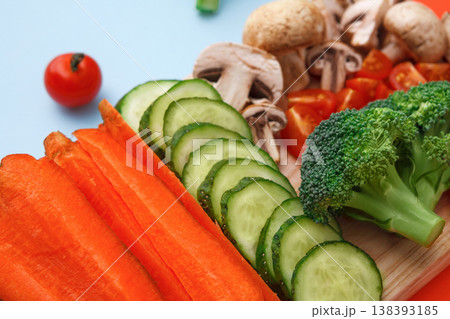 Healthy food background. Cut raw vegetables on wooden board. Chopped and sliced ingredients for salad or soup - mushroom, cherry tomato, broccoli, cucumber, carrot on bright background 138393185