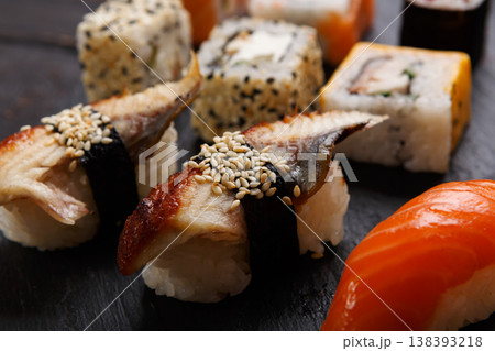 Sushi and rolls closeup. Japanese restaurant delivery. Salmon, unagi, california and other healthy meals on dark wooden background Sushi and rolls closeup. Japanese restaurant delivery. Salmon, unagi, california and other healthy meals on dark wooden background 138393218