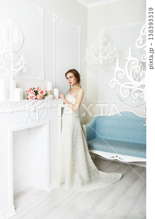 Wedding dress fashion. Beautiful young bride in vintage wedding dress indoors. White wedding dress at model. Girl shows wedding fashion in decorated shabby chic interior with flowers, high key. Wedding dress fashion. Beautiful young bride in vintage wedding dress indoors. White wedding dress at model. Girl shows wedding fashion in decorated shabby chic interior with flowers, high key. 138393319