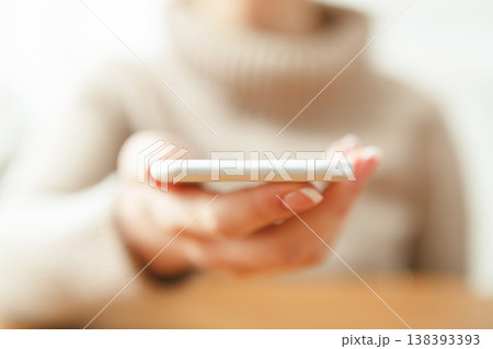 Female holding smartphone while sitting at wooden table, selective focus, close up. 138393393