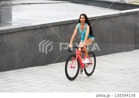 Sexy girl with bicycle. Young slim sexy sporty woman in blue shorts and white snickers long-haired, sensual riding at pink fix bicycle in urban city environment. Soft toned. 138394138