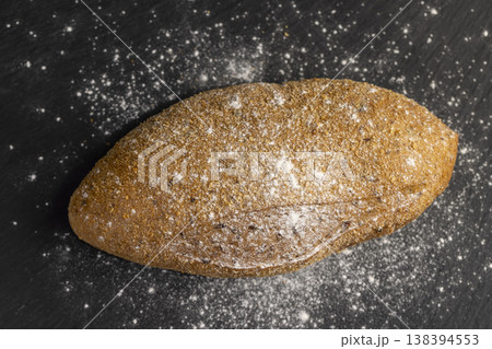 a fresh soft loaf of bread on black slate, a baked soft loaf of rye bread lies on the table a fresh soft loaf of bread on black slate, a baked soft loaf of rye bread lies on the table 138394553