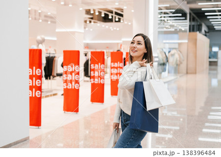 Happy Woman Carrying Shopping Bags Stands in Bright Mall Aisle Happy Woman Carrying Shopping Bags Stands in Bright Mall Aisle 138396484