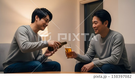 リビングでビールを注ぎながら父をねぎらう息子と親子の温かい時間（AI生成） 138397082