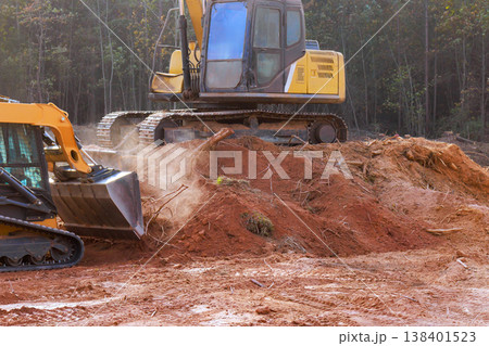 Two machines work on construction site, moving dirt debris in forested area 138401523