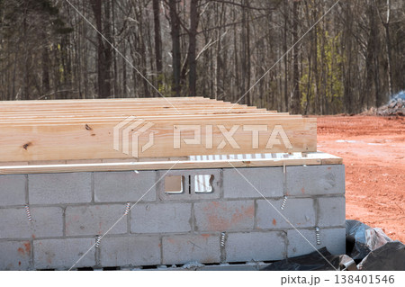 Wooden beams sit top concrete blocks at new building site in leafless wooded area. 138401546