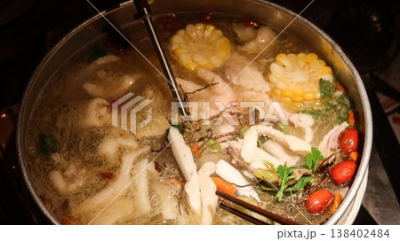 close up of a Chinese hot pot with boiling soup with corn, red dates, herbs, greens, Cordyceps Flower and chicken with chopsticks and large spoon close up of a Chinese hot pot with boiling soup with corn, red dates, herbs, greens, Cordyceps Flower and chicken with chopsticks and large spoon 138402484
