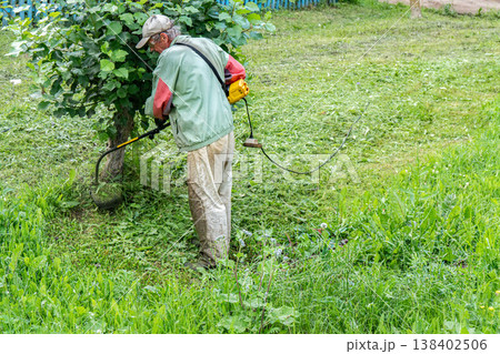 Elderly man mows grass with electric trimmer in front of his home Elderly man mows grass with electric trimmer in front of his home 138402506