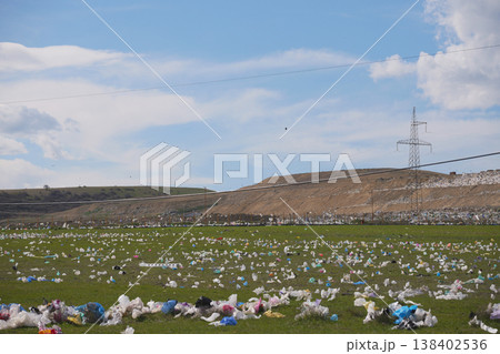 Wide shot of colorful plastic bags littering a green field near a large industrial landfill 138402536