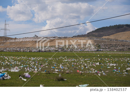 Wide shot of colorful plastic bags littering a green field near a large industrial landfill 138402537