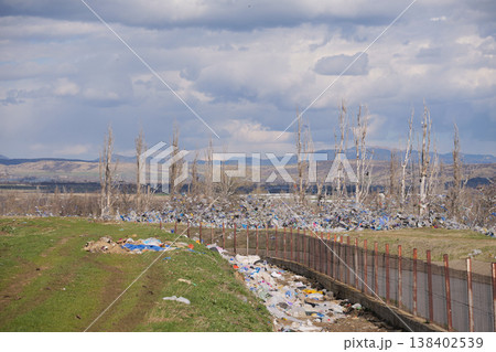 Wide shot of colorful plastic bags littering a green field near a large industrial landfill 138402539