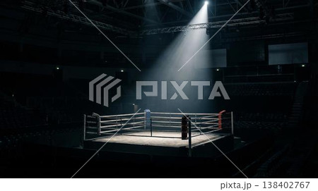 Boxing ring illuminated by a spotlight in an empty arena, with seating visible in the background and a dark atmosphere enhancing the scene's intensity 138402767