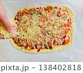 Process of making homemade pizza top view with person hand adding ingredients on raw dough with ham vegetables and cheese on baking sheet domestic kitchen cooking hobby handmade meal preparation 138402818