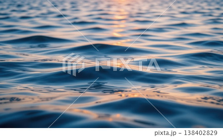 Macro shot of gentle blue sea ripples with golden sunlight reflecting on the water surface at dusk. 138402829