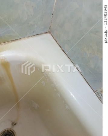 Dirty bathtub with heavy rust stains, yellow grime, mold along caulk, calcium buildup and peeling paint on surrounding tiles, showing severe neglect and unsanitary conditions Dirty bathtub with heavy rust stains, yellow grime, mold along caulk, calcium buildup and peeling paint on surrounding tiles, showing severe neglect and unsanitary conditions 138402948