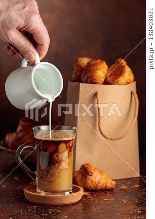 Coffee latte and paper bag with croissants on a brown background. Coffee latte and paper bag with croissants on a brown background. 138403021