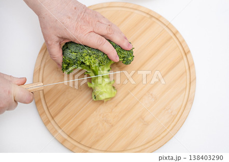 Cutting fresh broccoli on a wooden cutting board, close-up of healthy food preparation in the kitchen Cutting fresh broccoli on a wooden cutting board, close-up of healthy food preparation in the kitchen 138403290