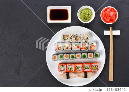 Traditional japanese food restaurant. Colorful sushi set served on white platter with chopsticks, soy sauce, ginger and wasabi. Top view on gray background with copy space Traditional japanese food restaurant. Colorful sushi set served on white platter with chopsticks, soy sauce, ginger and wasabi. Top view on gray background with copy space 138403442