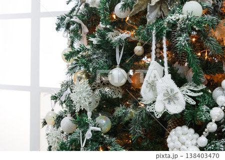 Winter holidays atmosphere background. Closeup of beautifully decorated fir tree with modern shiny baubles, beards, garland and small knitted mittens . Christmas and new year magic at home, copy space Winter holidays atmosphere background. Closeup of beautifully decorated fir tree with modern shiny baubles, beards, garland and small knitted mittens . Christmas and new year magic at home, copy space 138403470