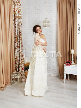 Wedding dress fashion. Beautiful young bride in vintage wedding dress indoors. White wedding dress at model. Girl shows wedding fashion in decorated shabby chic interior with flowers, high key. Wedding dress fashion. Beautiful young bride in vintage wedding dress indoors. White wedding dress at model. Girl shows wedding fashion in decorated shabby chic interior with flowers, high key. 138403495