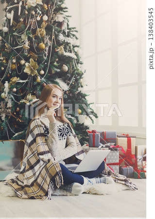 Young woman with credit card shopping online on laptop in cozy christmas interior. Girl in casual sitting under pine tree among lots of presents. Preparing to xmas, bying on winter sales. Copy space Young woman with credit card shopping online on laptop in cozy christmas interior. Girl in casual sitting under pine tree among lots of presents. Preparing to xmas, bying on winter sales. Copy space 138403545