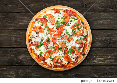 Delicious pizza with mushrooms, tomatoes and chicken ham - thin pastry crust at wooden round desk and rustic wood background. Italian food. Top view 138403584