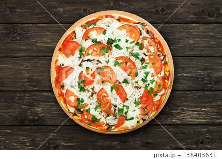 Delicious pizza with mushrooms, tomatoes and chicken meat - thin pastry crust at wooden round desk and rustic wood background. Italian food. Top view Delicious pizza with mushrooms, tomatoes and chicken meat - thin pastry crust at wooden round desk and rustic wood background. Italian food. Top view 138403631