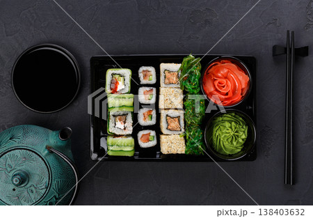 Japanese restaurant delivery, take away box top view, sushi maki and roll set. Chopsticks, ginger, soy sauce, wasabi. Meals at black background Japanese restaurant delivery, take away box top view, sushi maki and roll set. Chopsticks, ginger, soy sauce, wasabi. Meals at black background 138403632